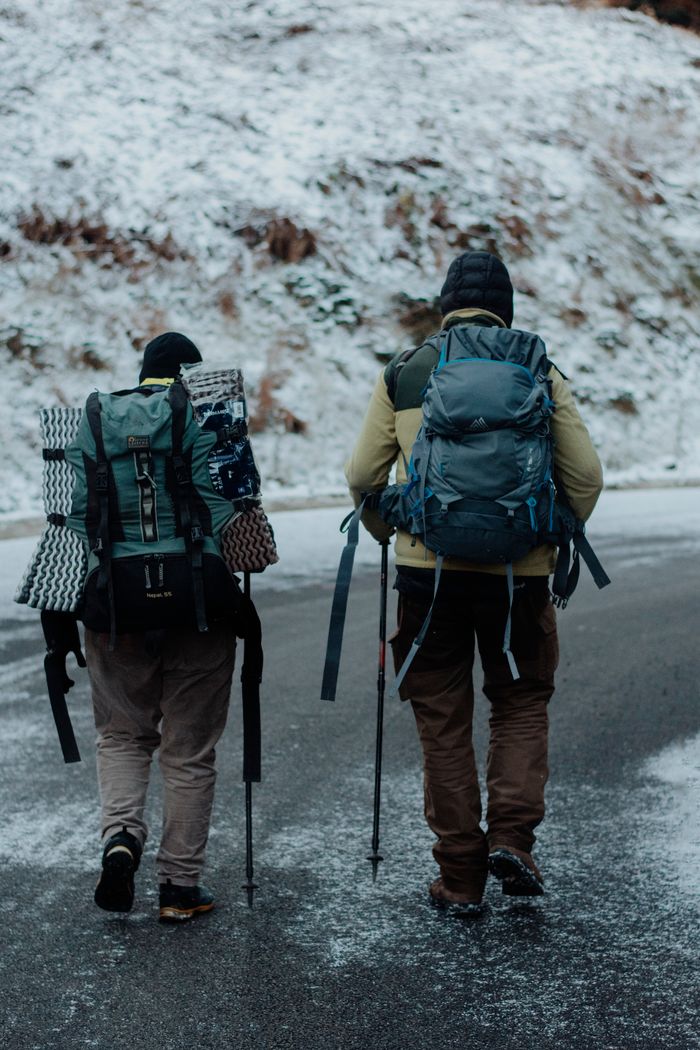 Services Two hikers with backpacks walking on a snowy road during winter, showcasing adventure and exploration.